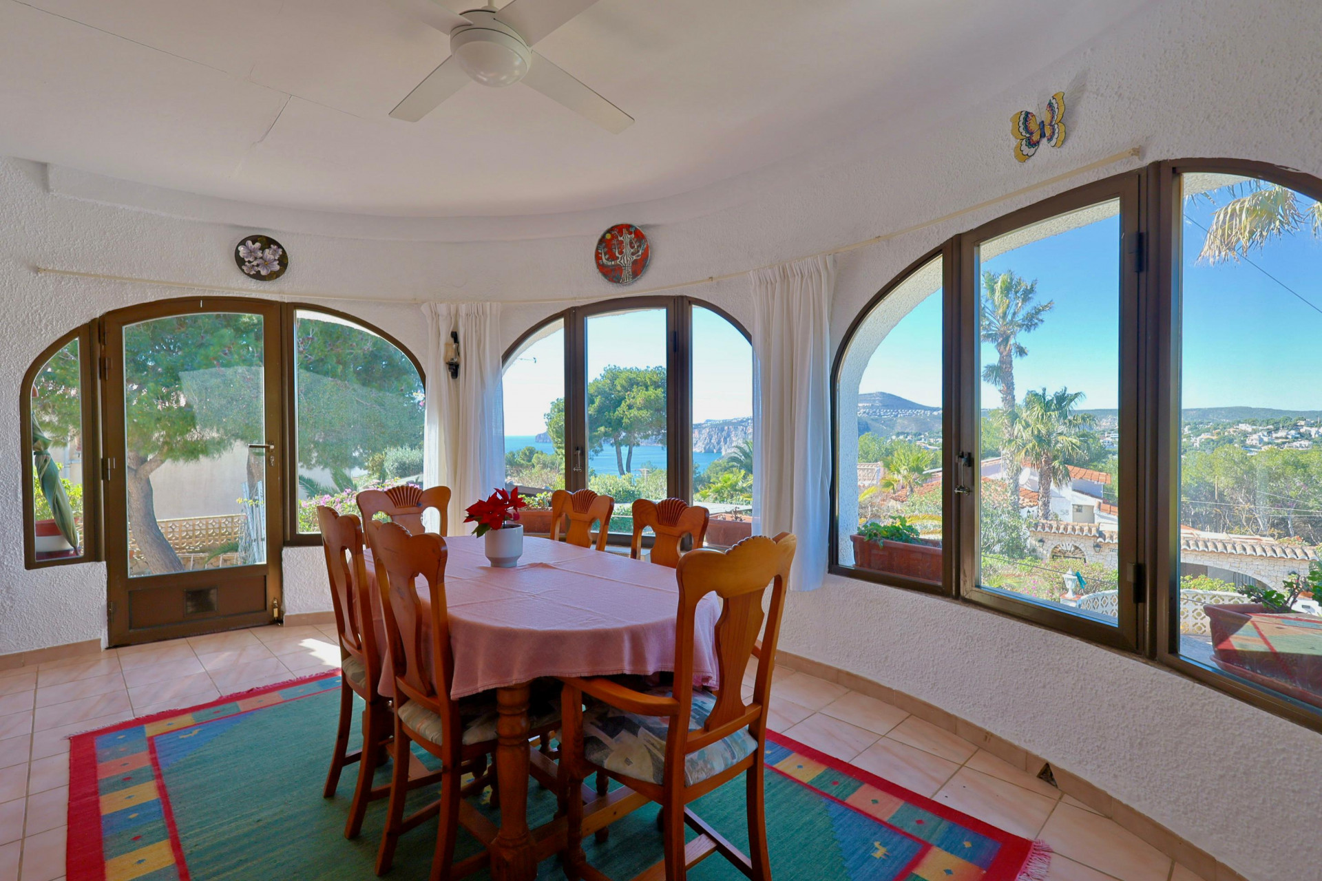 Bright dining room with sea views through arched windows. Wooden table with pink tablecloth.