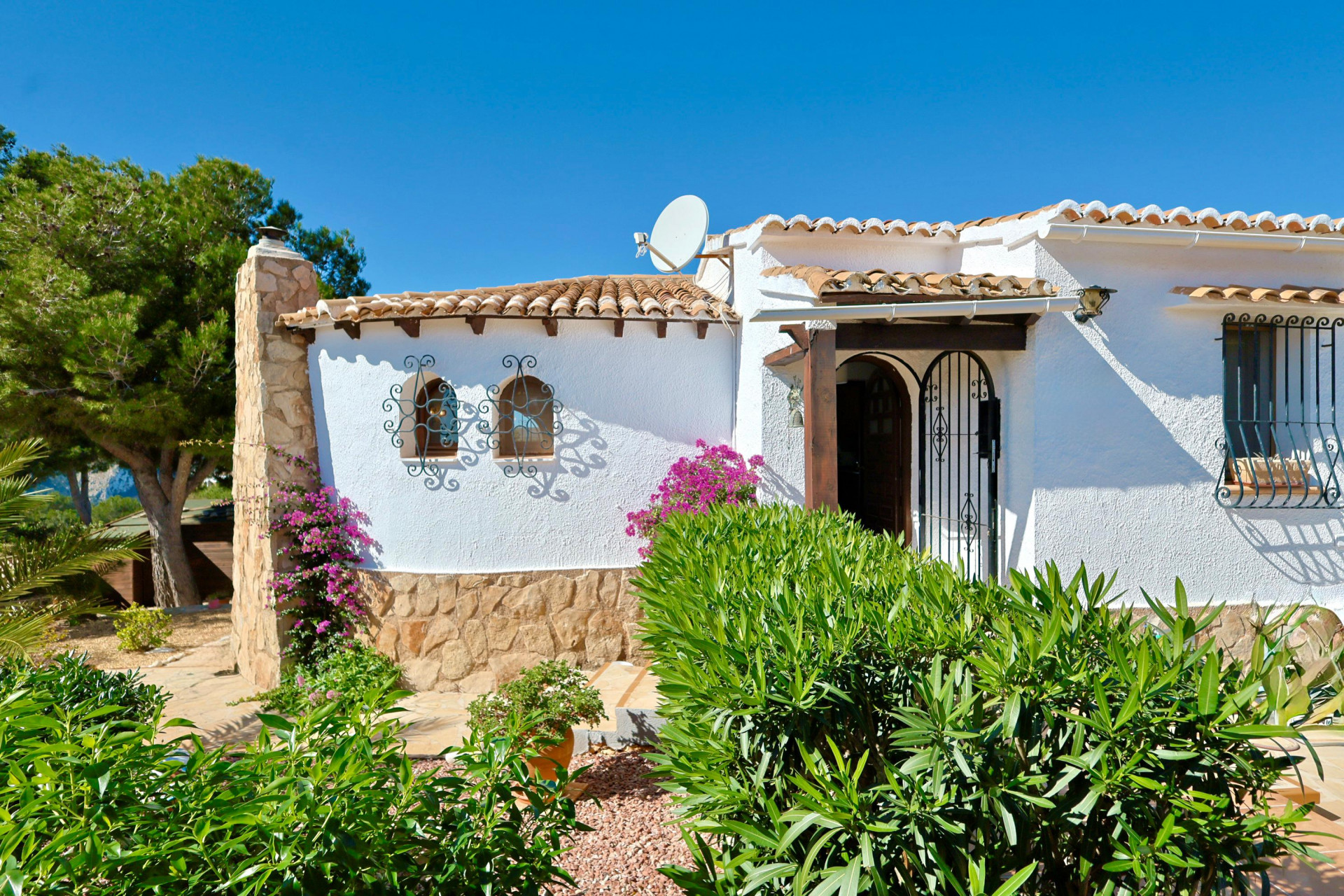 Facade of a Mediterranean villa with stone details, roof tiles, and ornamental ironwork.