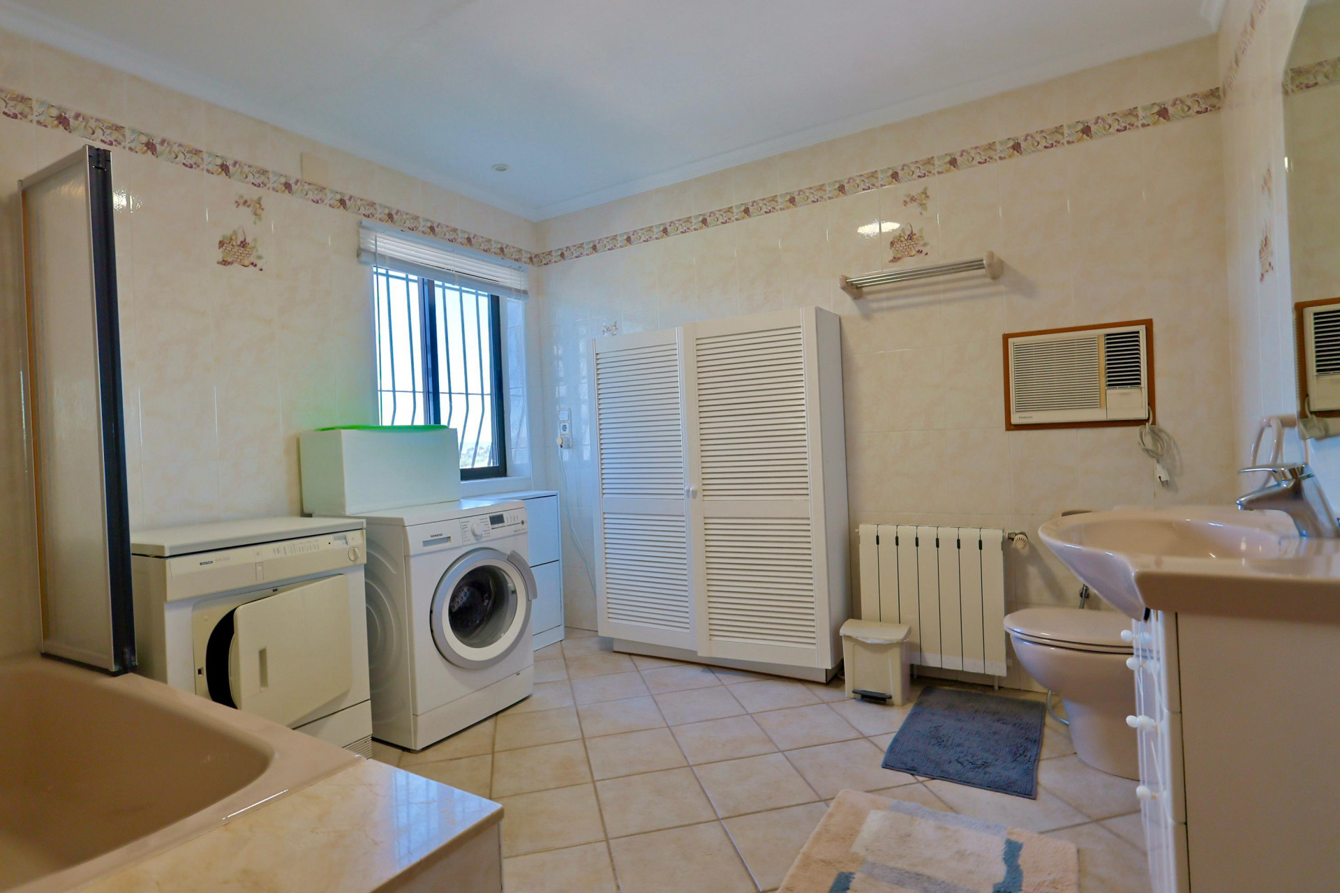 Functional bathroom featuring a washer, dryer, and a spacious white louvered cabinet.