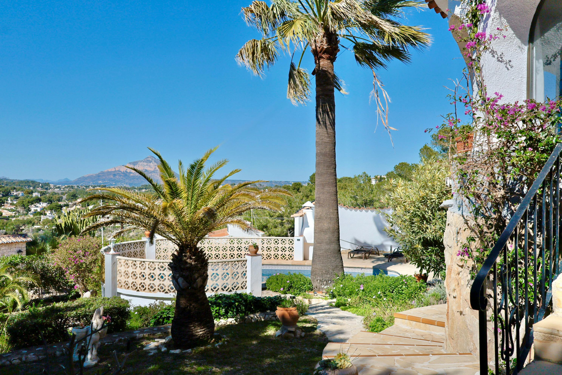 Garden view with pool and palm trees, highlighting the Mediterranean vegetation and mountain landscape in the background.