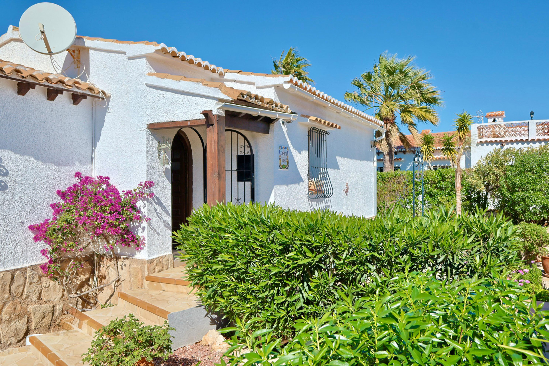 Mediterranean villa facade with bougainvillea and arched wood entrance.
