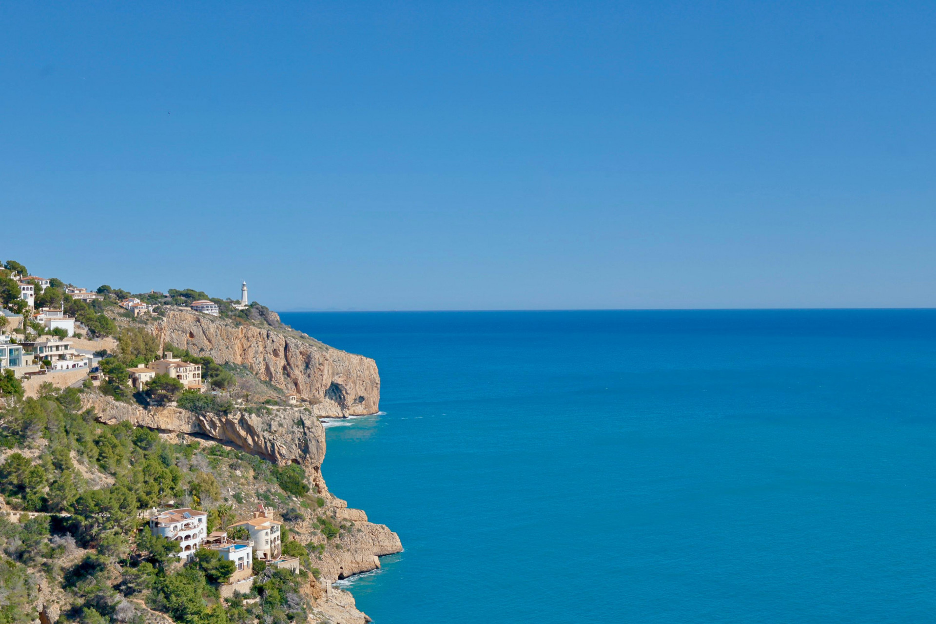 Panoramic view of the rocky coastline and Mediterranean Sea from Jávea, featuring white houses on the hillside.