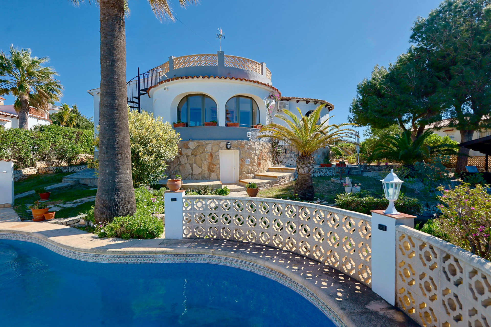 Pool view with lattice railing and stone facade of the villa in Jávea.