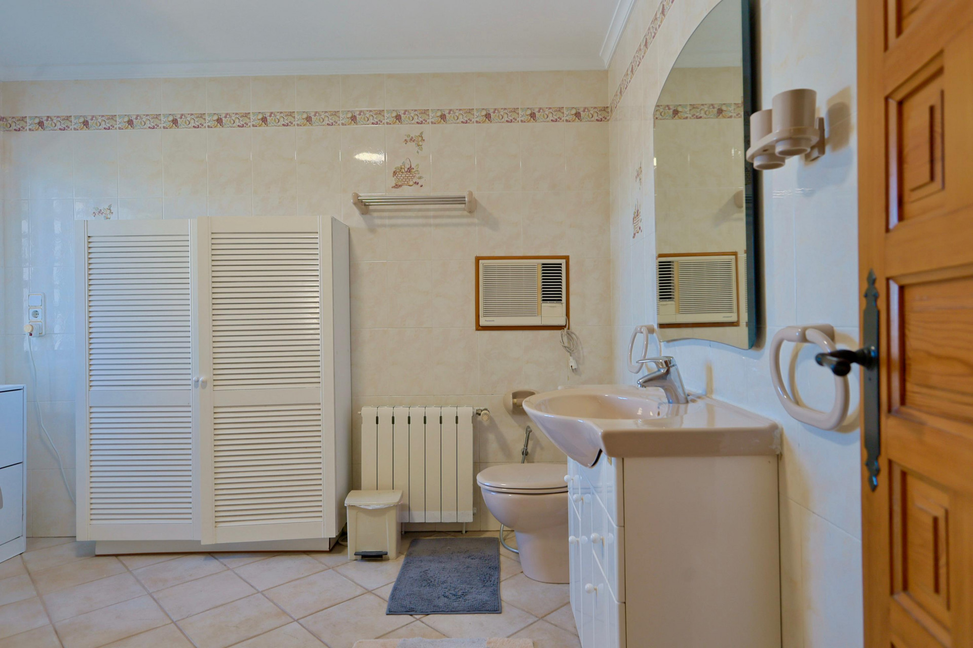 Tiled bathroom featuring a white louvered cabinet and a beige countertop sink.