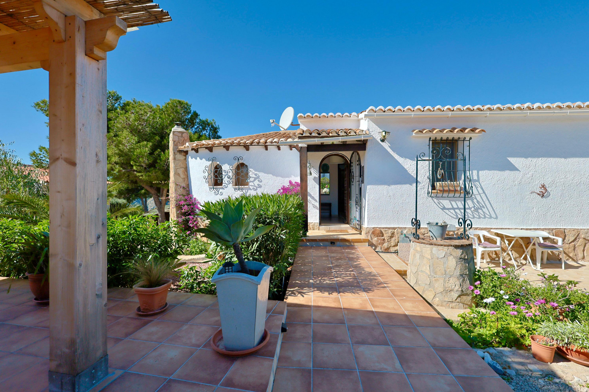 Villa entrance featuring a decorative well, garden, and tiled terrace.