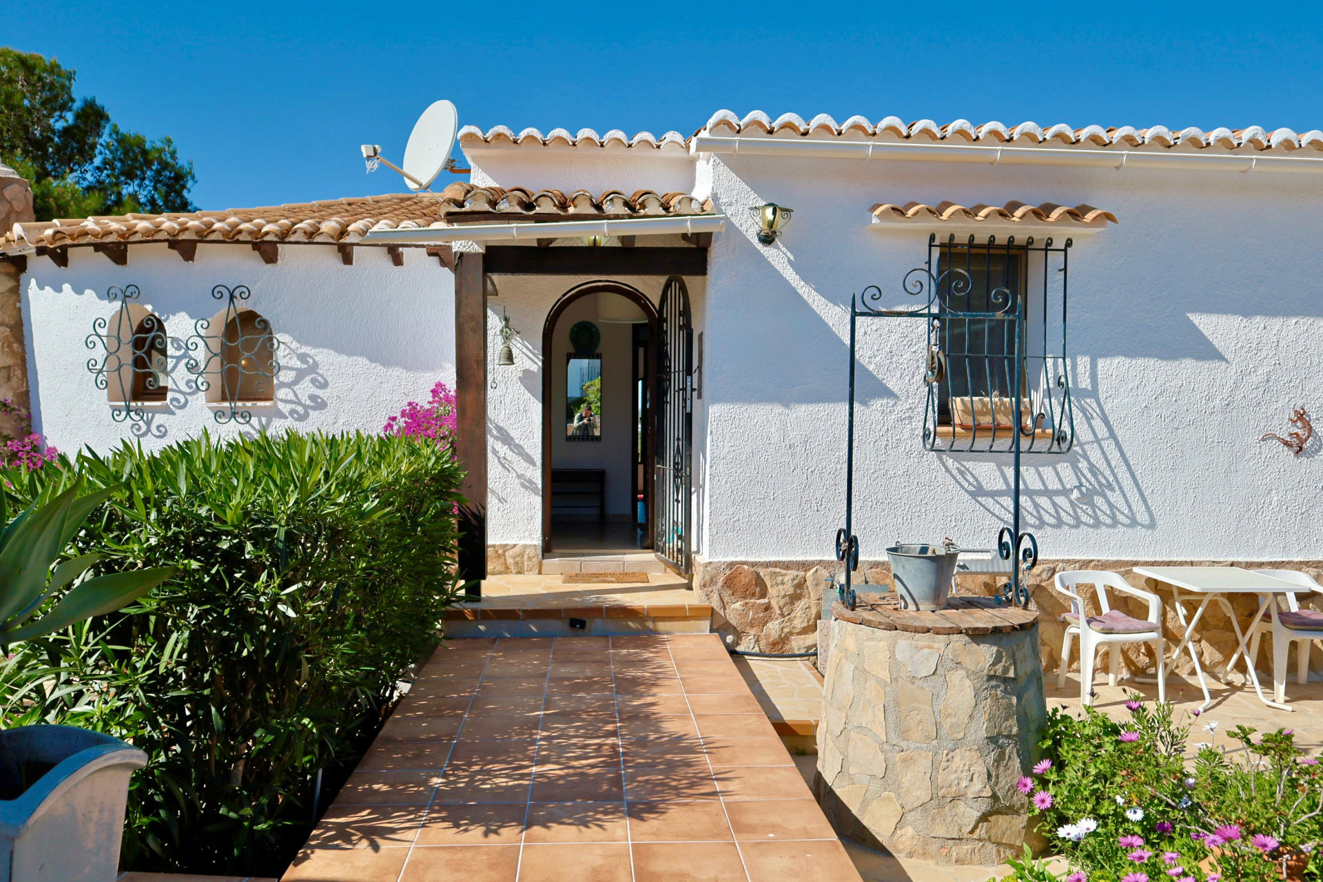 Villa entrance with stone well, tiled path, and textured white facade.