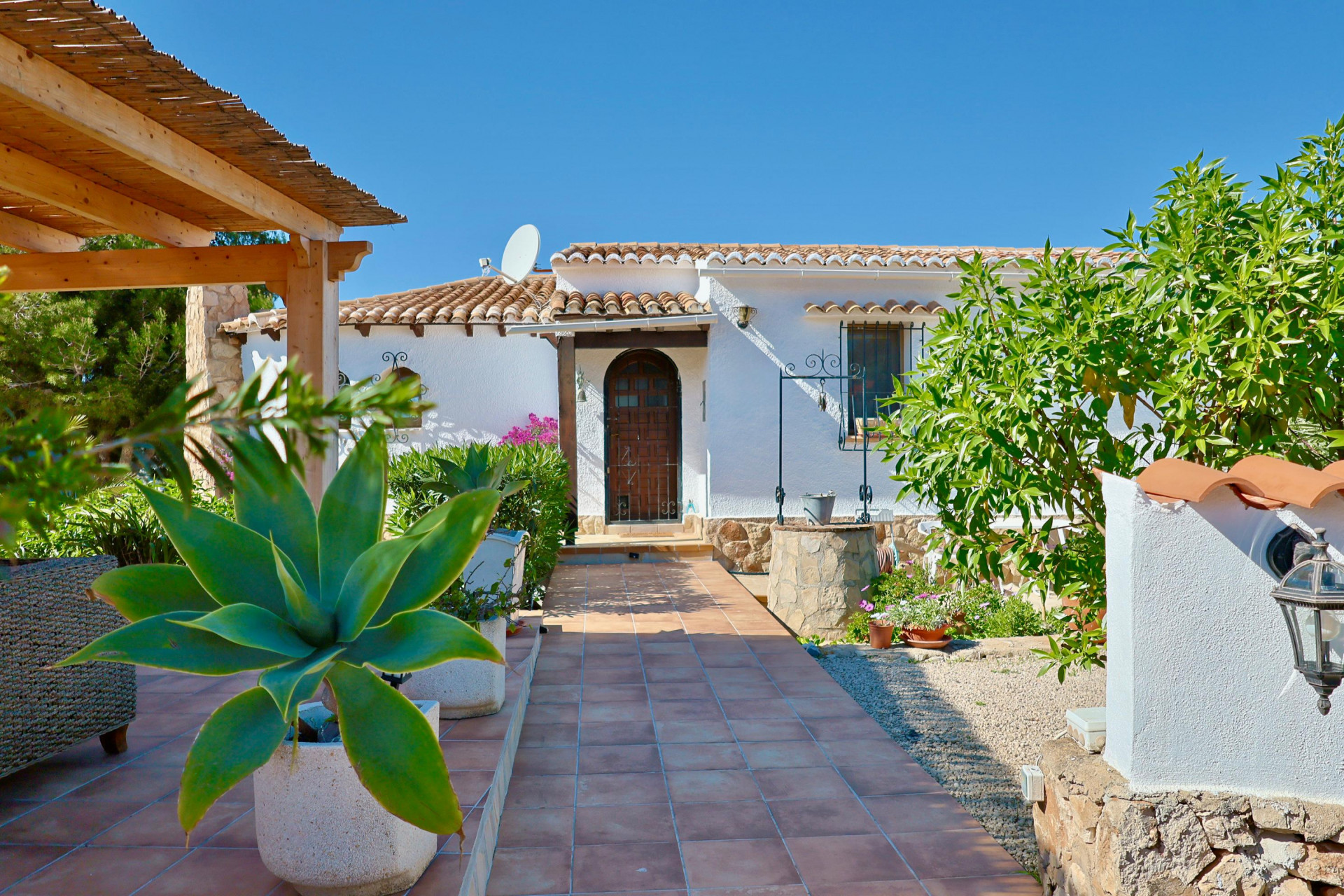 Villa entrance with tiled path, Mediterranean greenery, and a stone well.