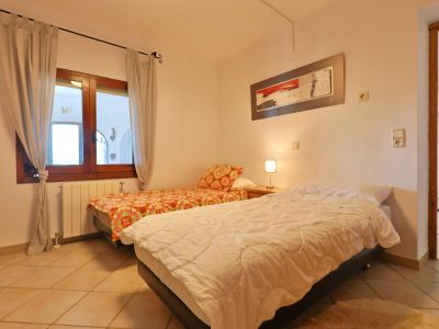 Bright bedroom featuring twin beds, a wooden window frame, and tiled flooring.