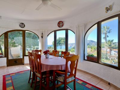 Bright dining room with sea views, surrounded by arched windows and rustic decor.