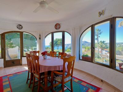 Bright dining room with sea views through arched windows. Wooden table with pink tablecloth.