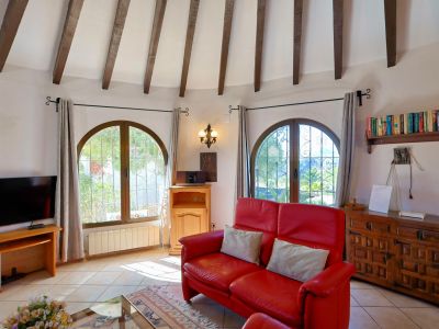 Bright living room featuring wood beams, a red leather sofa, and arched windows overlooking the garden.