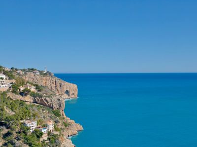 Panoramic view of the rocky coastline and Mediterranean Sea from Jávea, featuring white houses on the hillside.