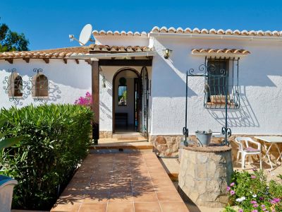 Villa entrance with stone well, tiled path, and textured white facade.