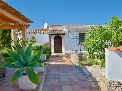 Villa entrance with tiled path, Mediterranean greenery, and a stone well.