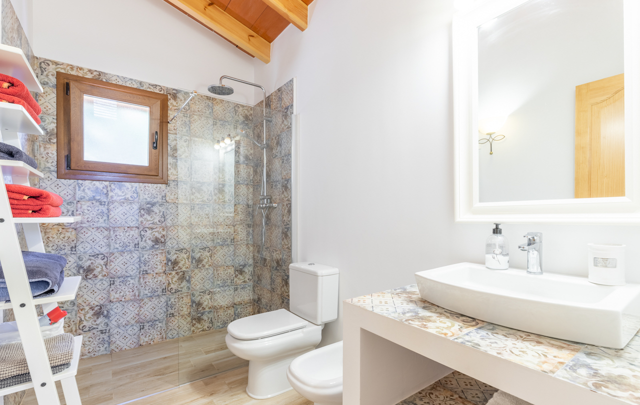 Bathroom featuring exposed wooden ceiling beams, a walk-in shower with patterned tiles, and a matching tiled vanity with a vessel sink and white fixtures.