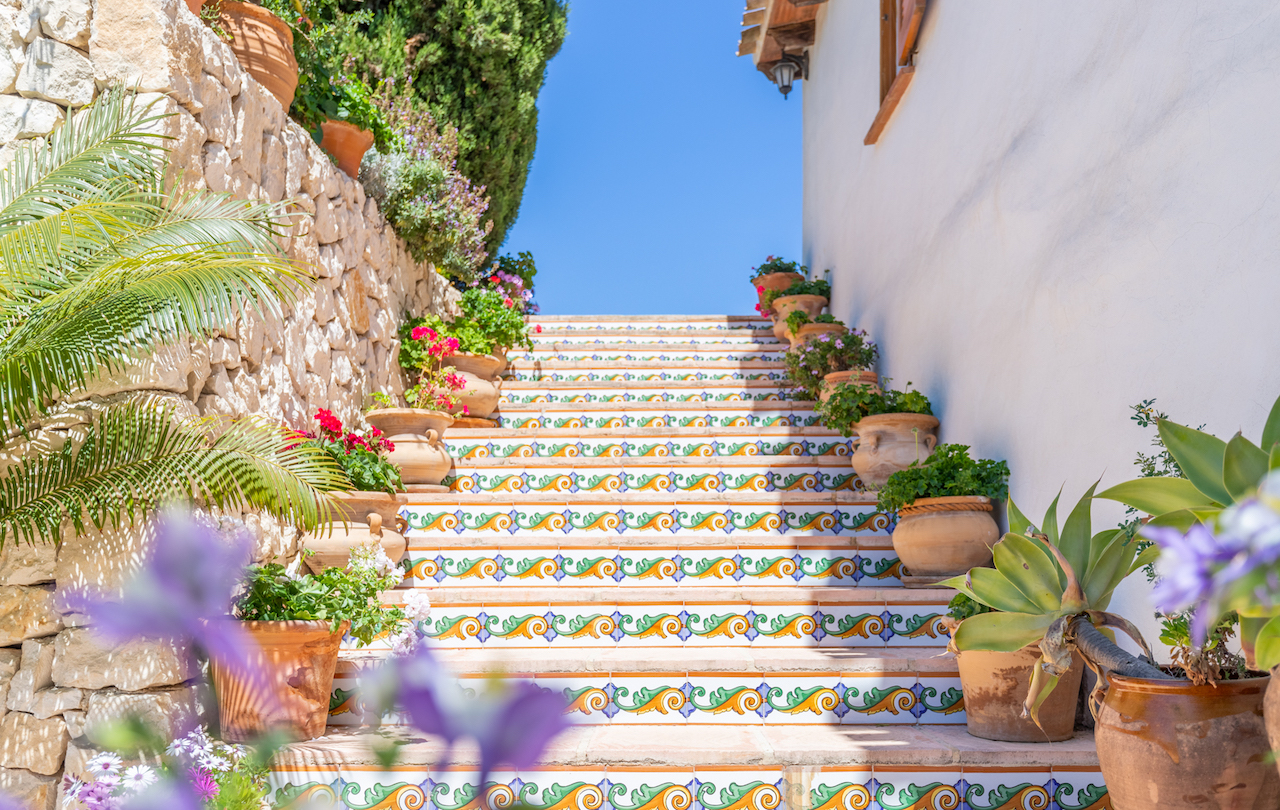 Exterior staircase featuring traditional hand-painted ceramic tiles on the risers, lined with terracotta planters and a natural dry stone wall.