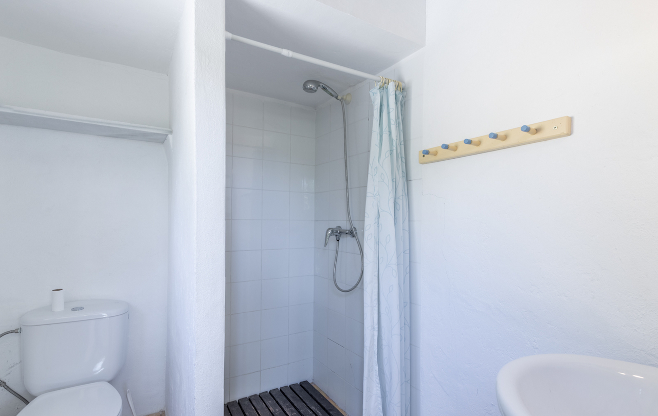 Functional bathroom featuring a tiled walk-in shower with a dark wood slat floor, a patterned curtain, and a wall-mounted wooden rack with blue pegs.