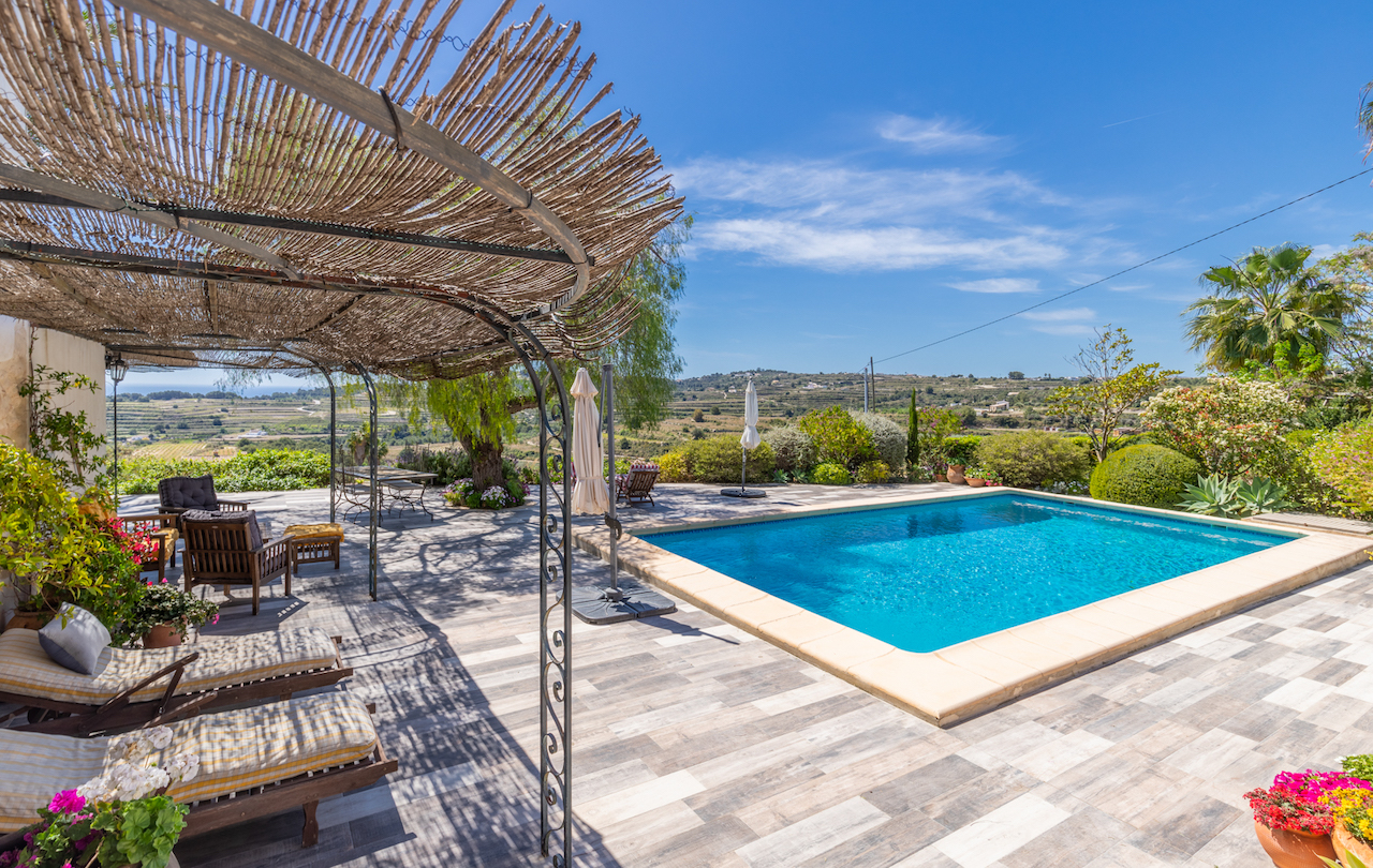 Outdoor pool area featuring a wrought iron pergola with a reed roof. The non-slip terrace offers panoramic valley views and integrated Mediterranean garden landscaping.