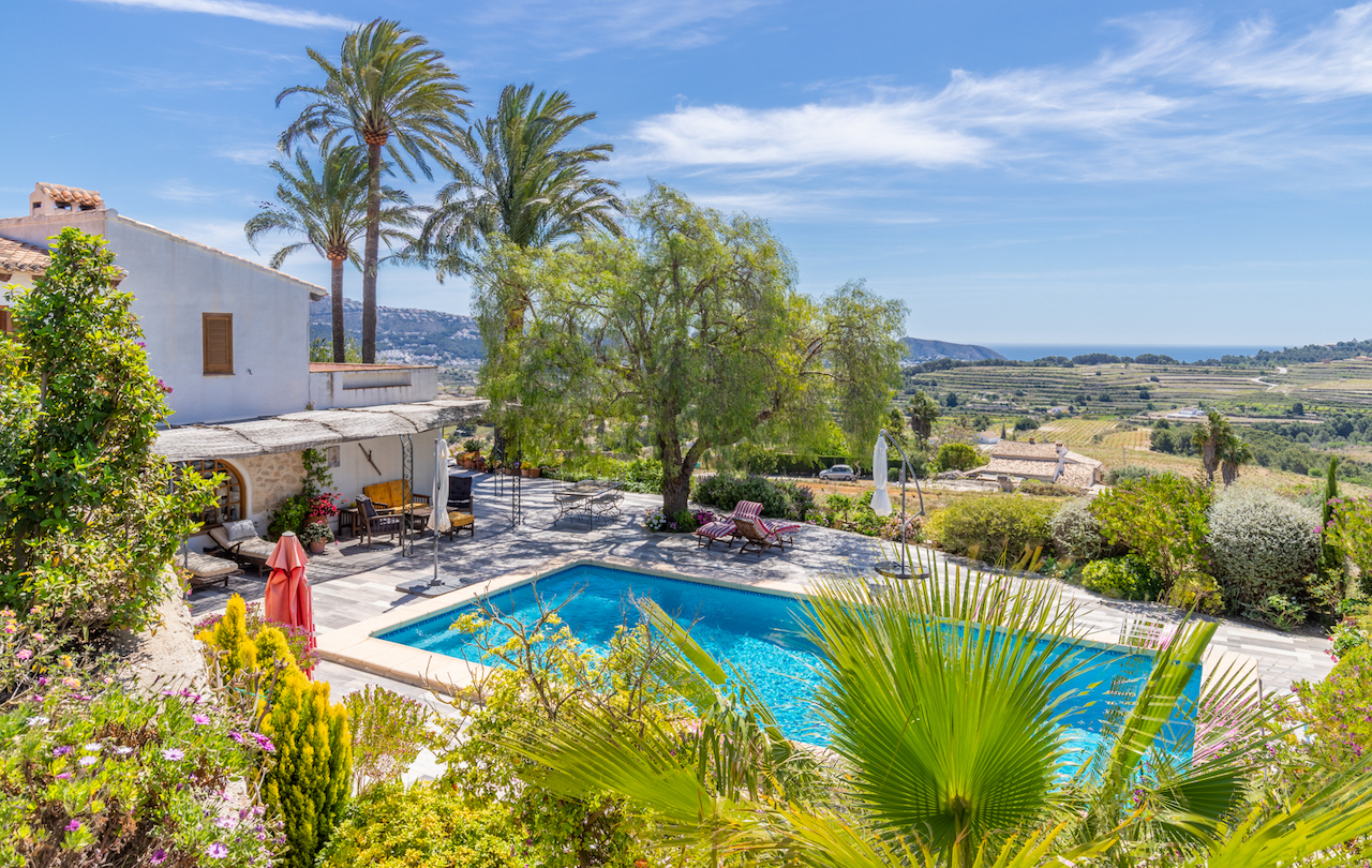 Outdoor swimming pool area featuring a stone terrace and Mediterranean landscaping with expansive views over coastal vineyards toward the sea.