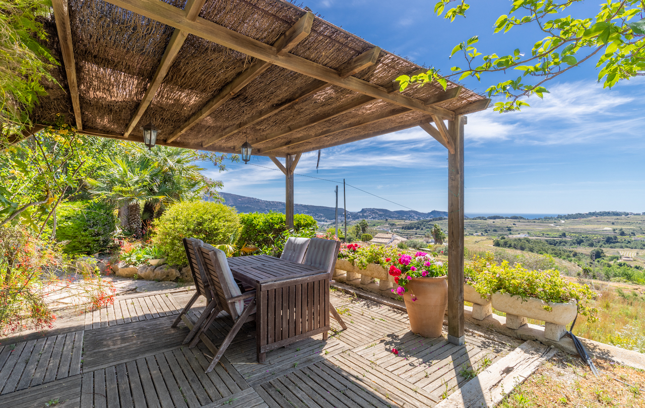 Outdoor terrace featuring a wooden pergola with heather roofing, a teak dining set, and panoramic views over the valley towards the Mediterranean Sea.