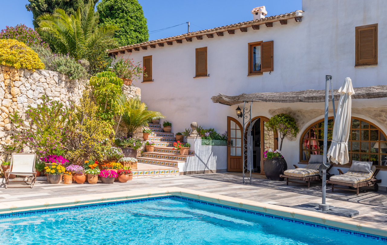 Pool area featuring a large non-slip terrace, white facade with wooden shutters, and exterior stairs decorated with traditional ceramic tiles.