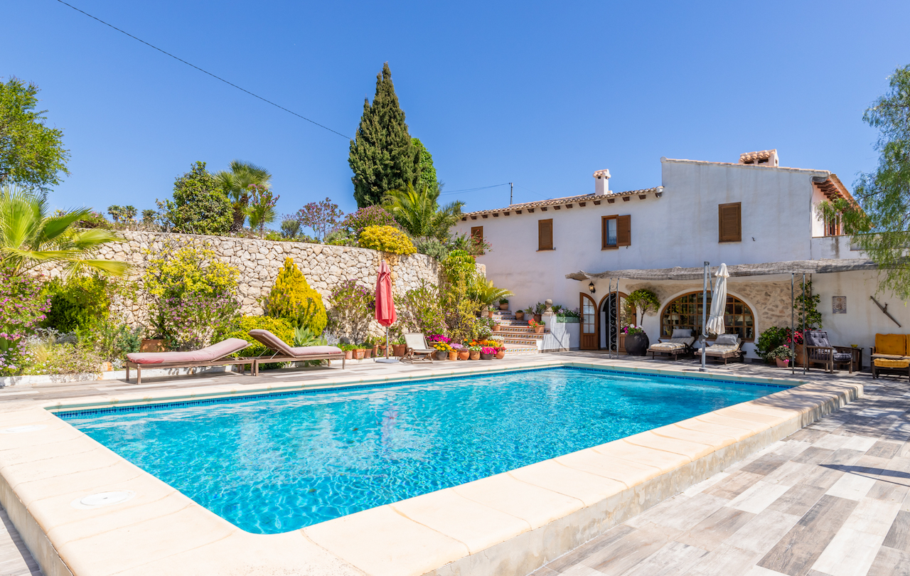 Rectangular swimming pool featuring a non-slip terrace, natural stone walls, and mature Mediterranean gardens adjacent to the traditional white-washed finca.