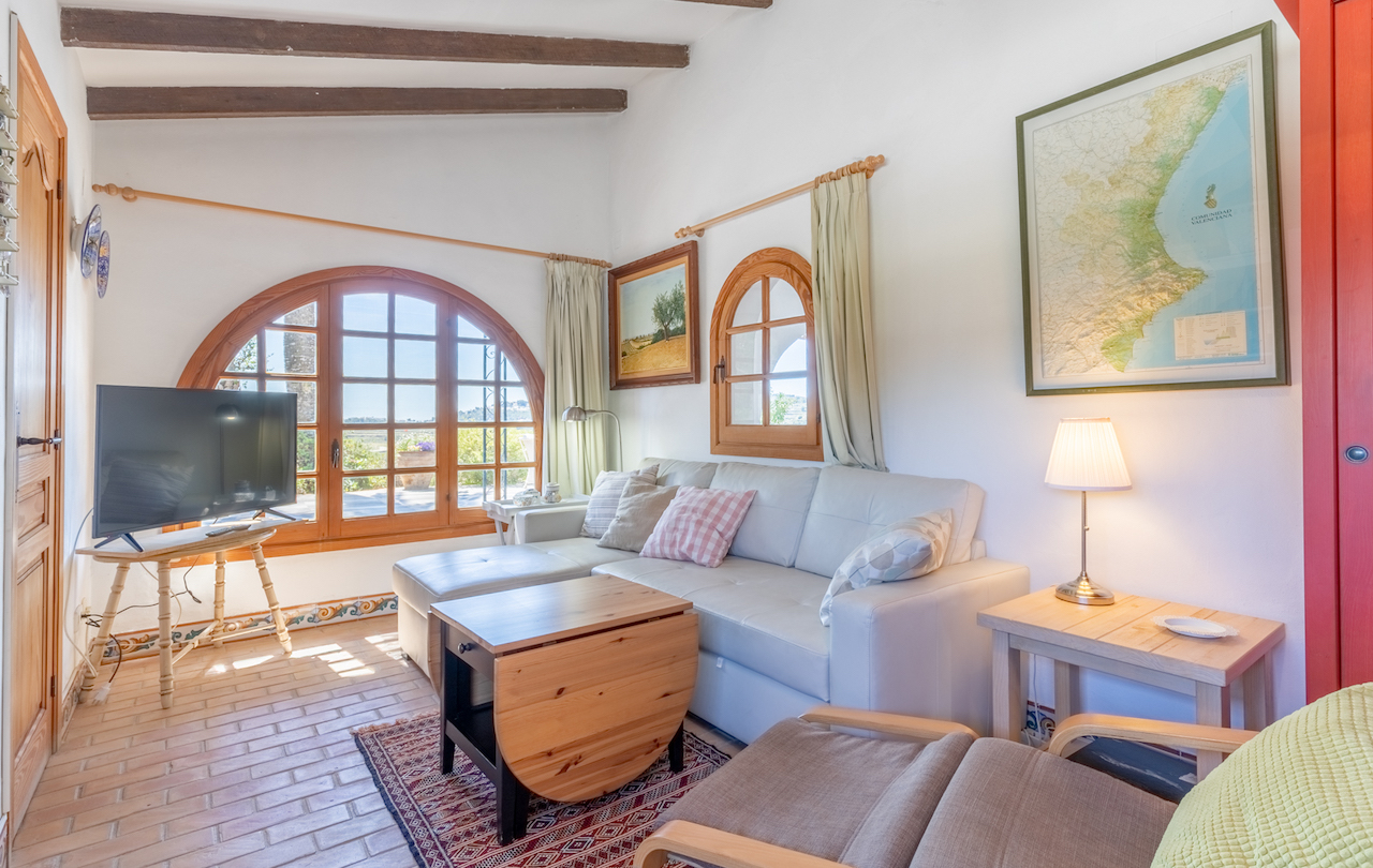 Rustic living area featuring exposed wooden beams, terracotta flooring, and arched timber windows that provide abundant natural light and garden views.