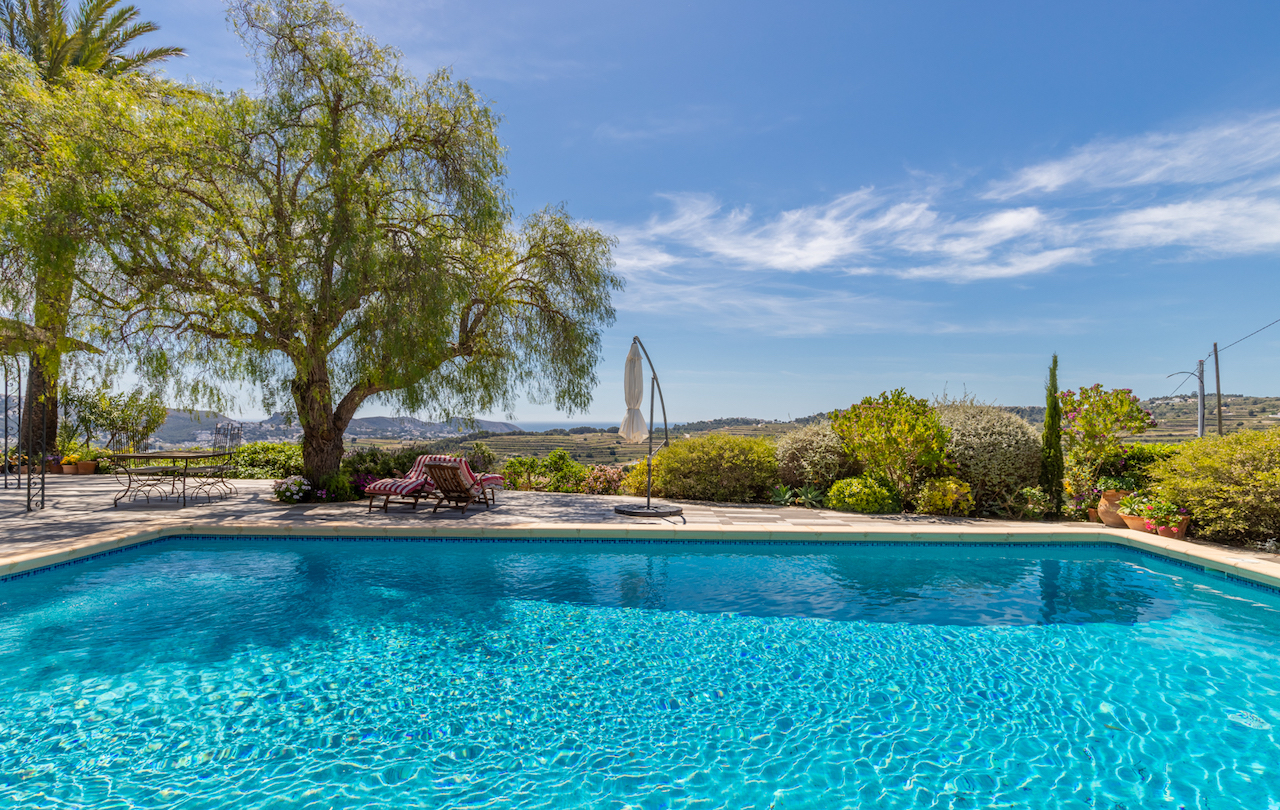 Spacious pool terrace with non-slip paving, shaded seating area under mature trees, and panoramic views over vineyards towards the Mediterranean.