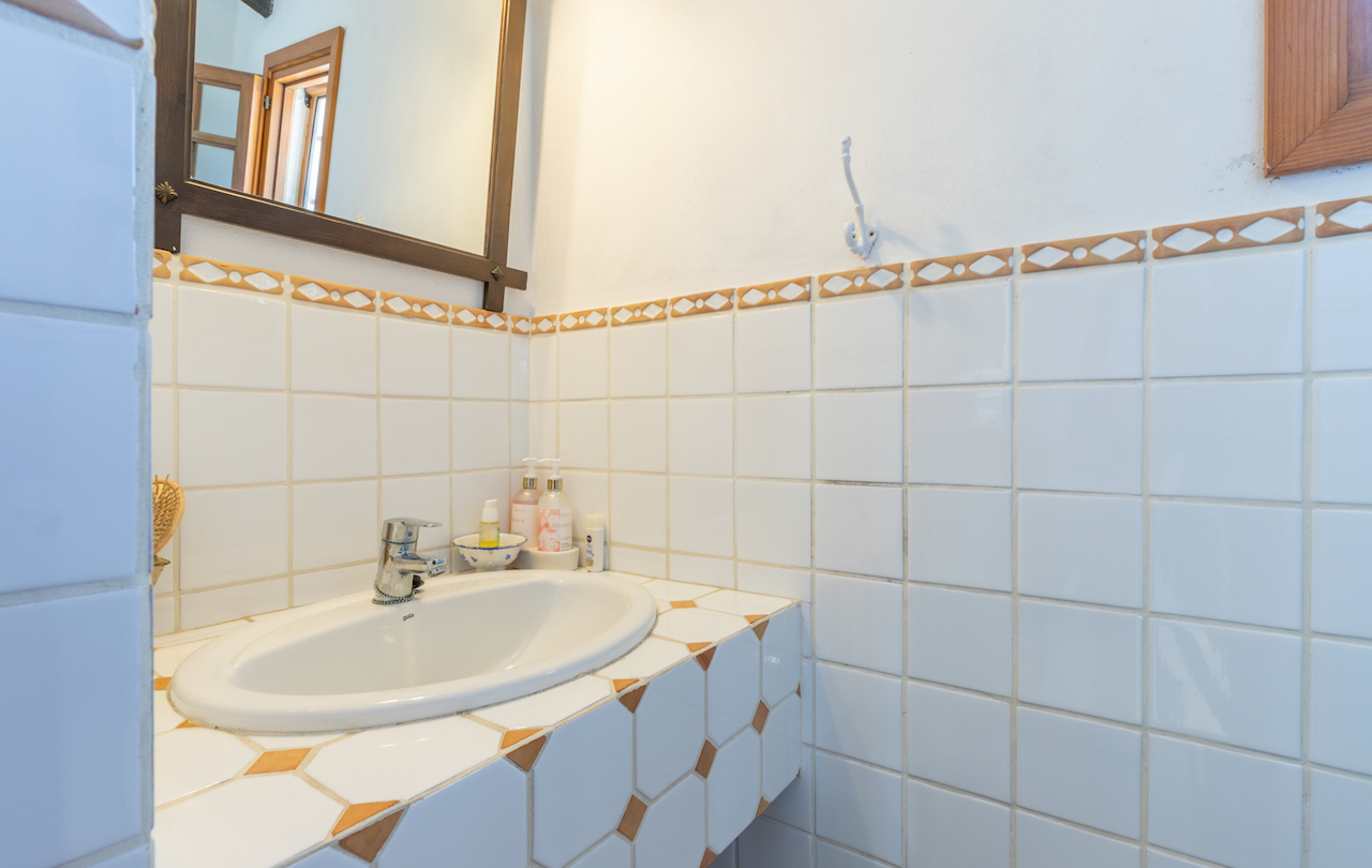 Traditional bathroom featuring white tiling with decorative borders. Includes an oval drop-in sink set into a tiled countertop with geometric patterns and a wooden-framed mirror.