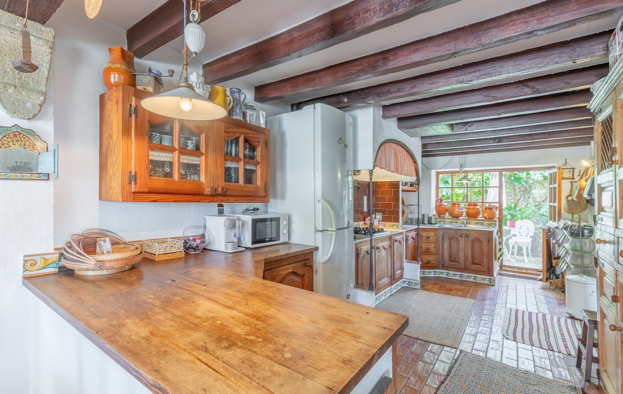 Traditional Valencian kitchen featuring exposed dark wood beams, solid wood countertops, and direct access to a lush garden patio.