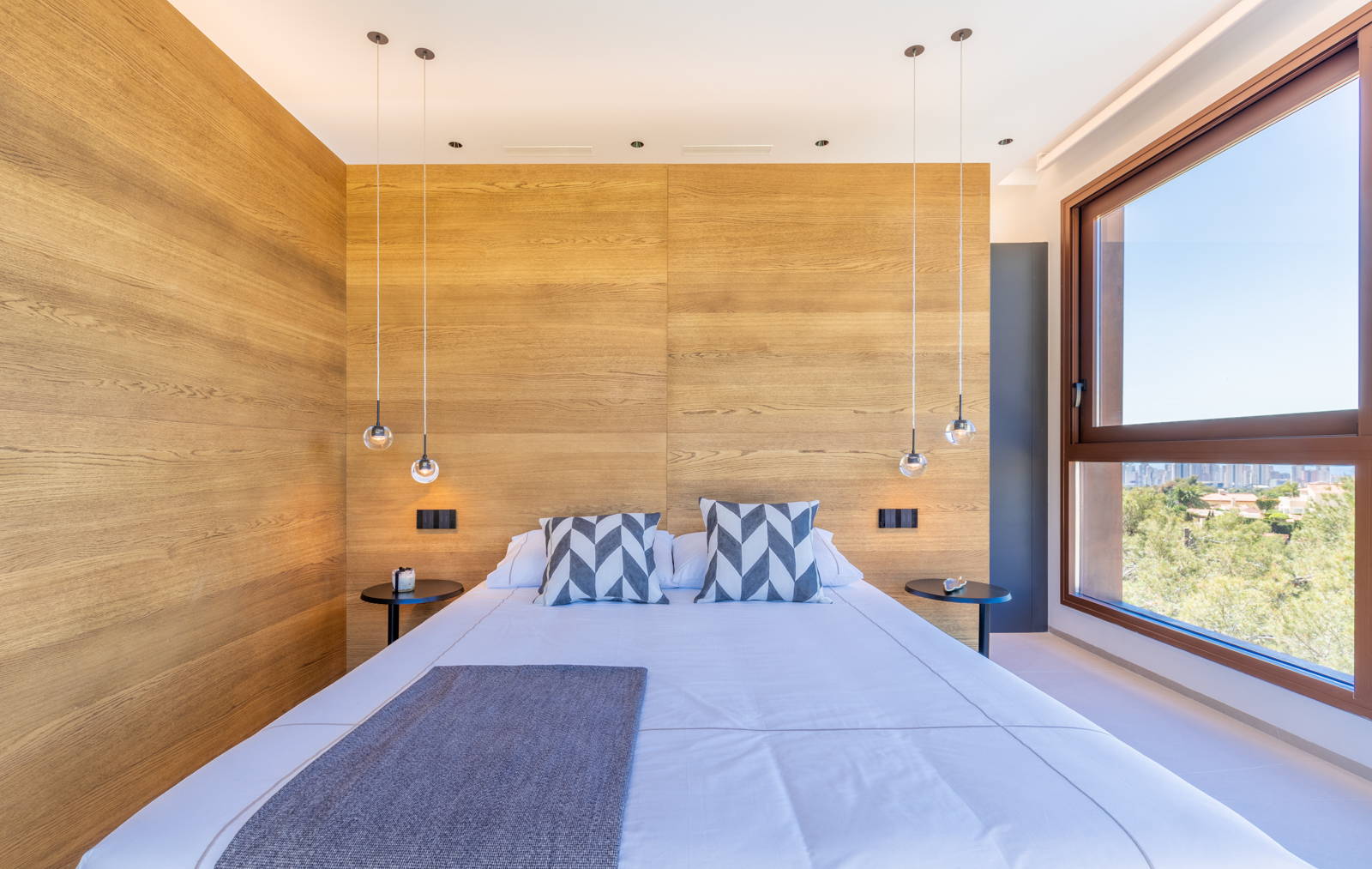 Bedroom with light wood wall, spherical pendant lights, and exterior views.