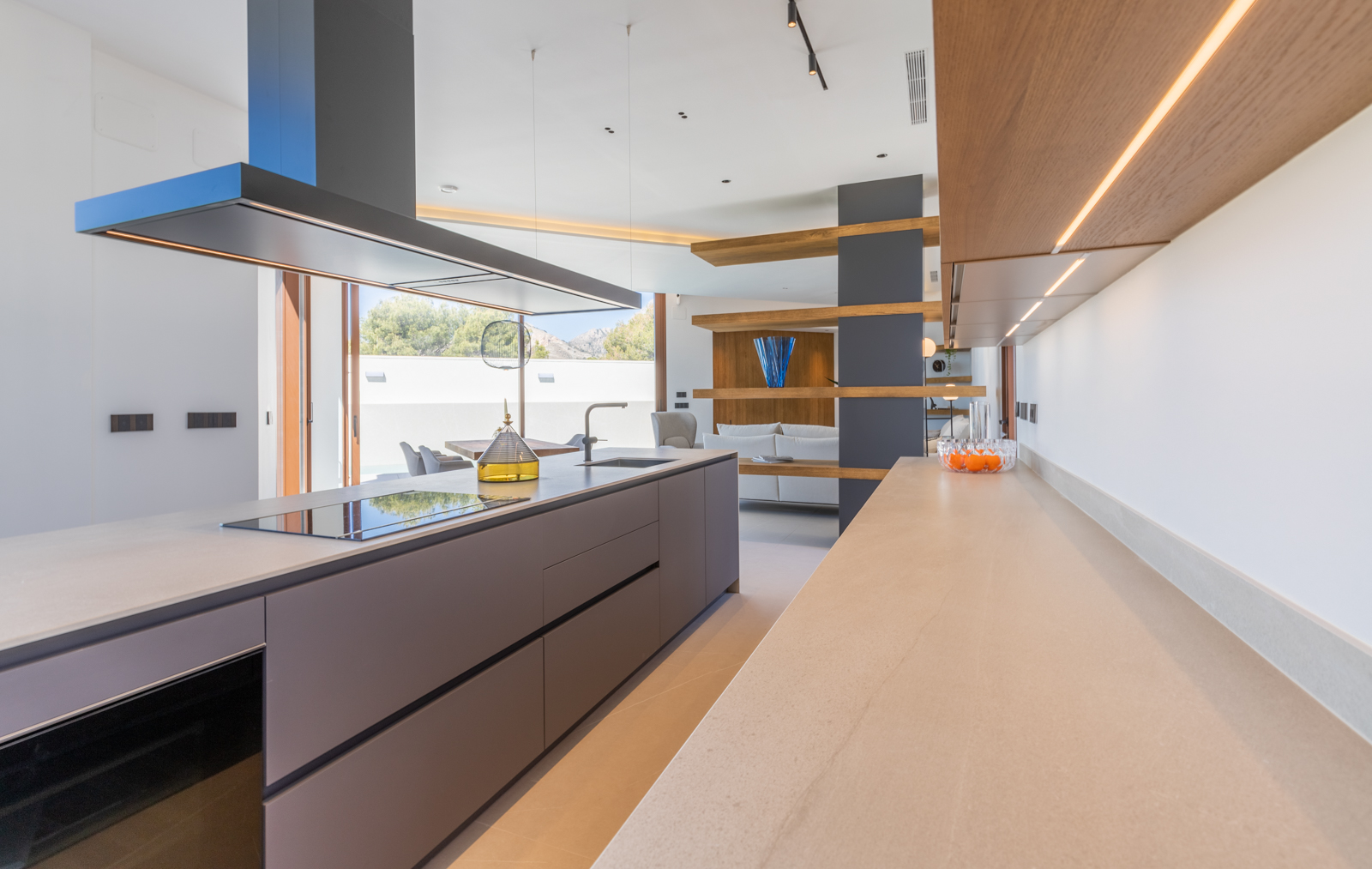 Detail of the modern kitchen with gray island, beige countertop, and illuminated wooden shelves.