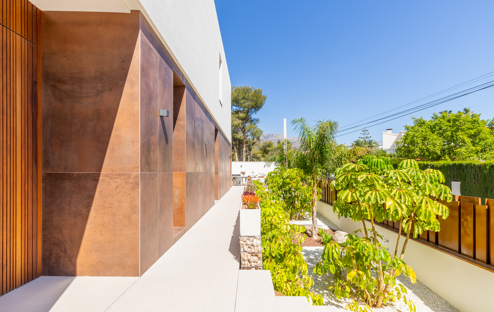 Exterior view of the villa with a Mediterranean garden and earth-toned clad wall.
