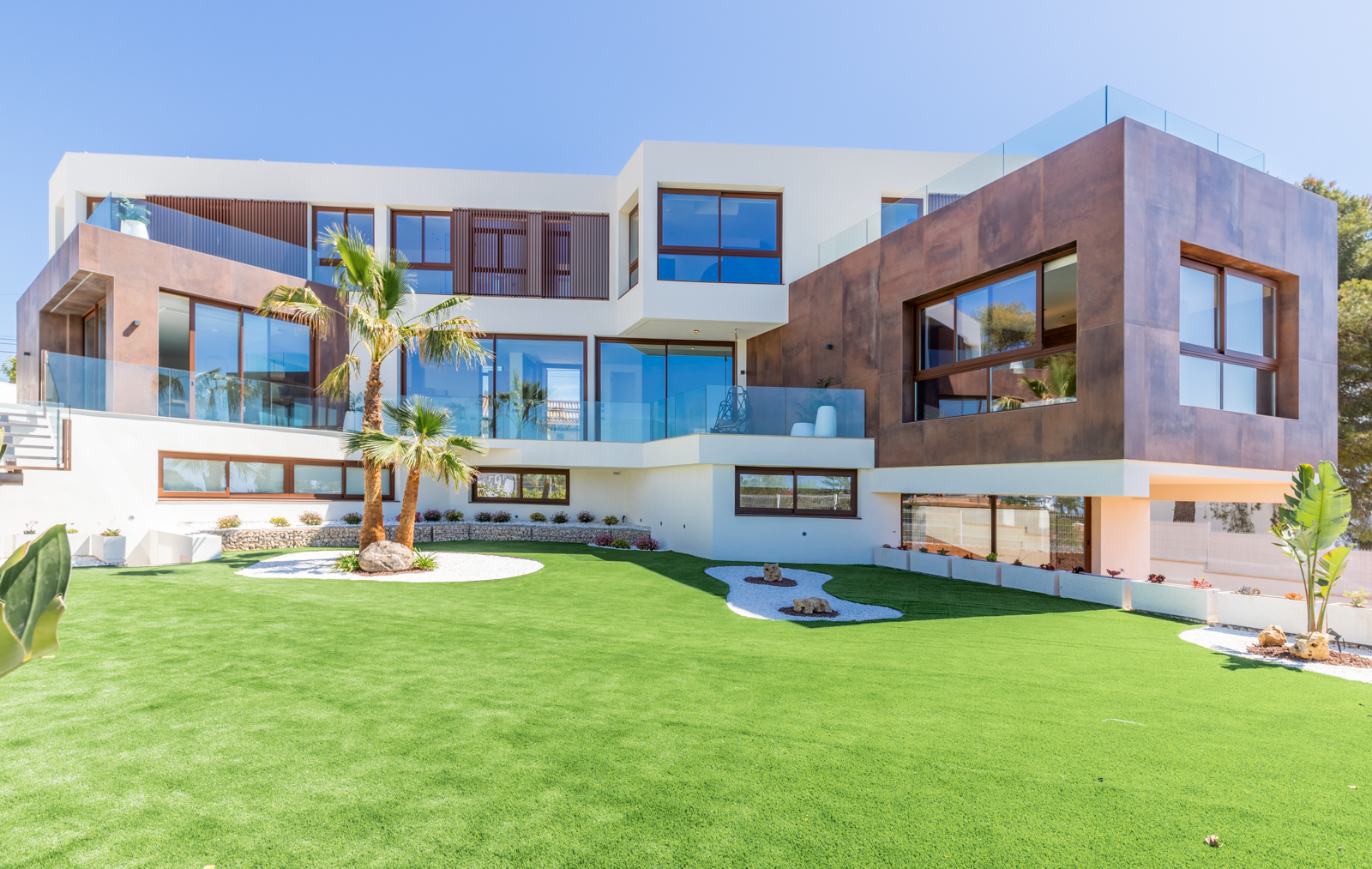 Exterior view of the villa with lawn garden, palm trees and a modern facade with large windows.