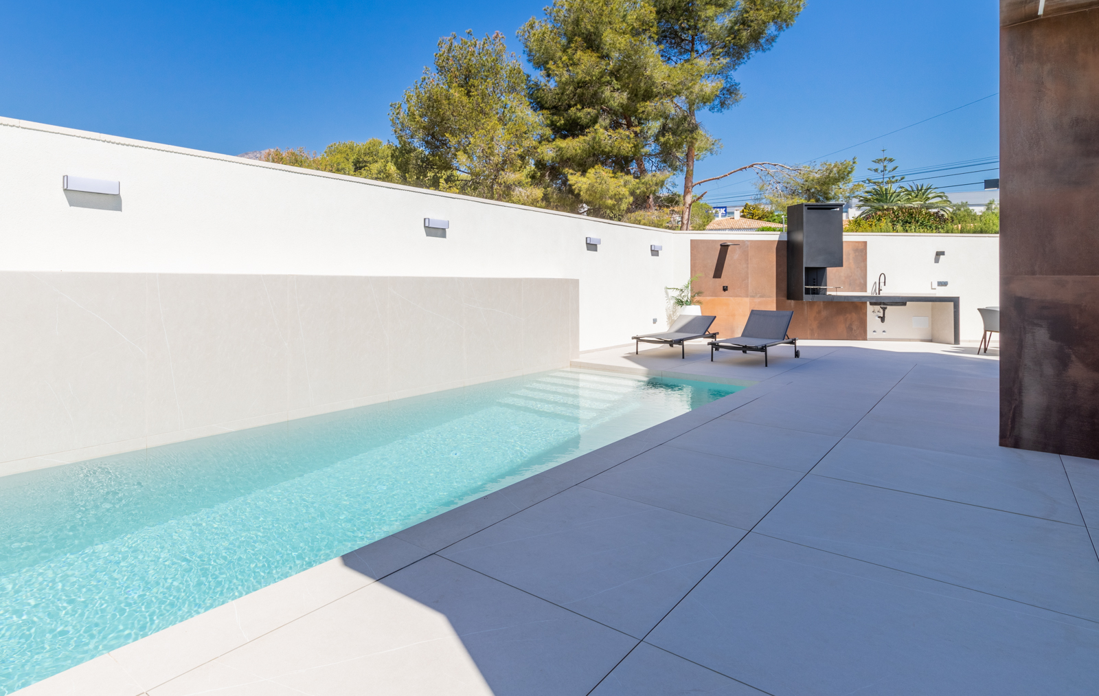 Modern pool featuring a white tiled wall and a barbecue area with a concrete countertop.