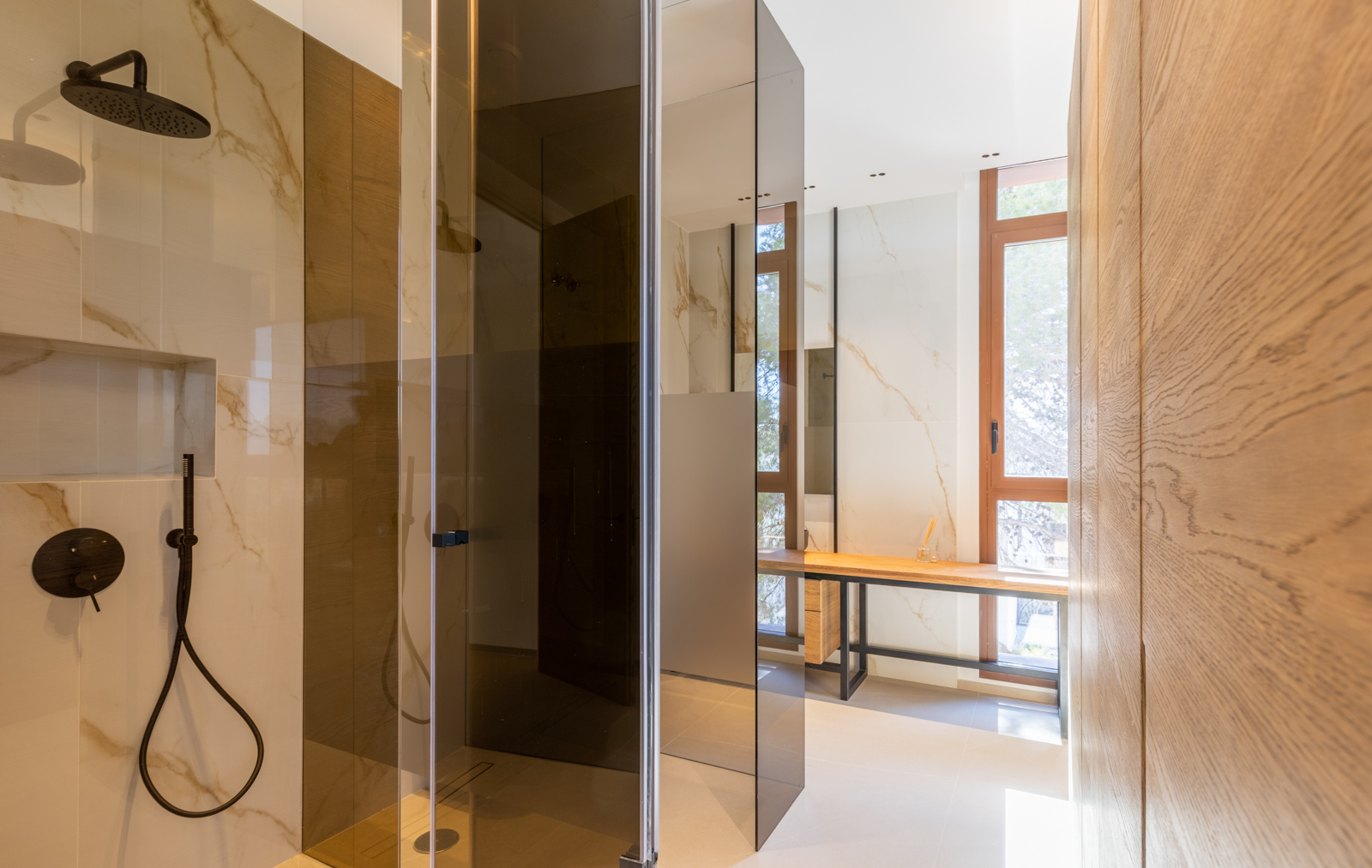 Shower detail with smoked glass and light wood vanity in a modern bathroom with veined tiles.