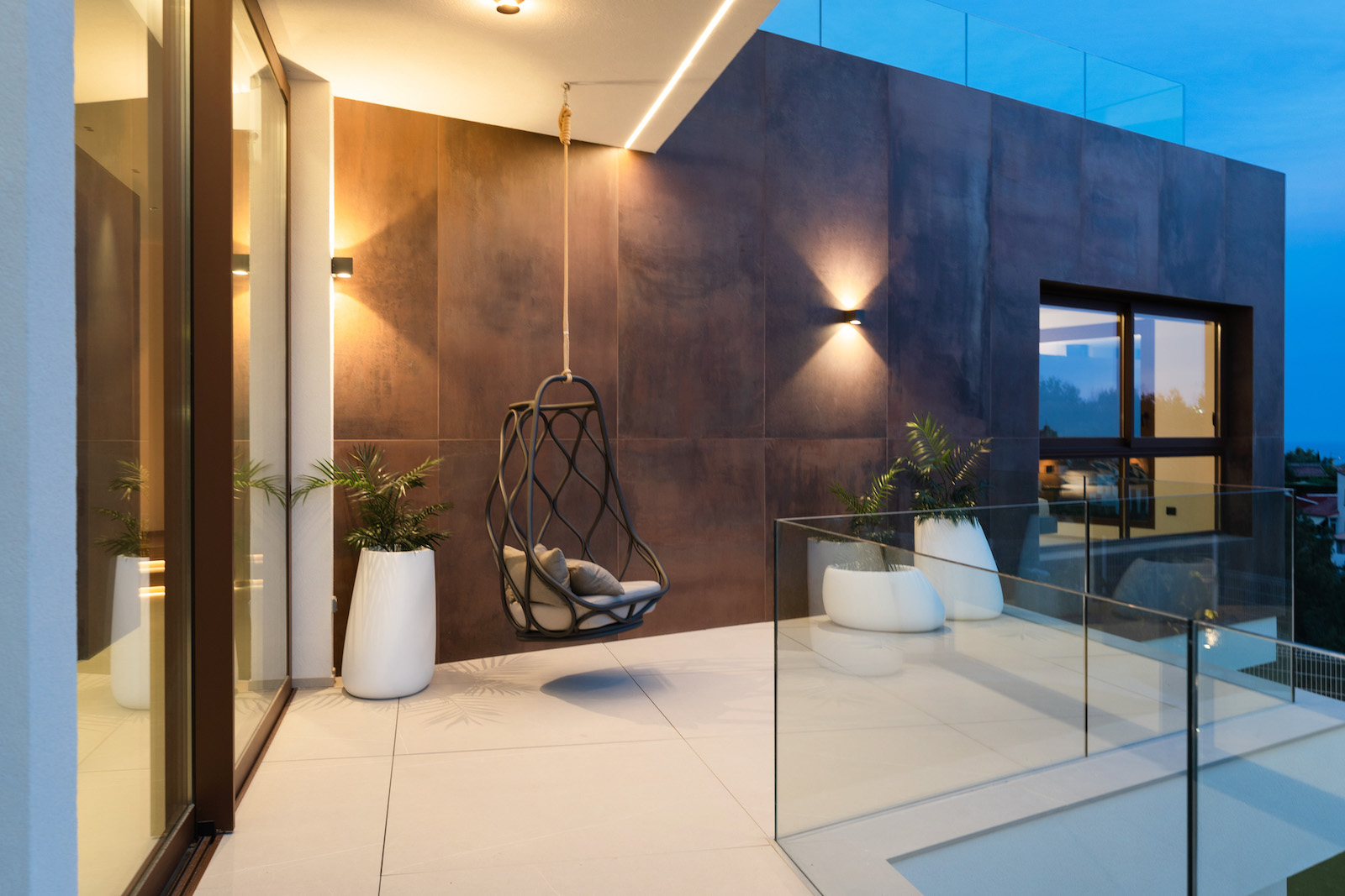 Terrace with rust-colored tile wall, hanging chair, and glass railing.