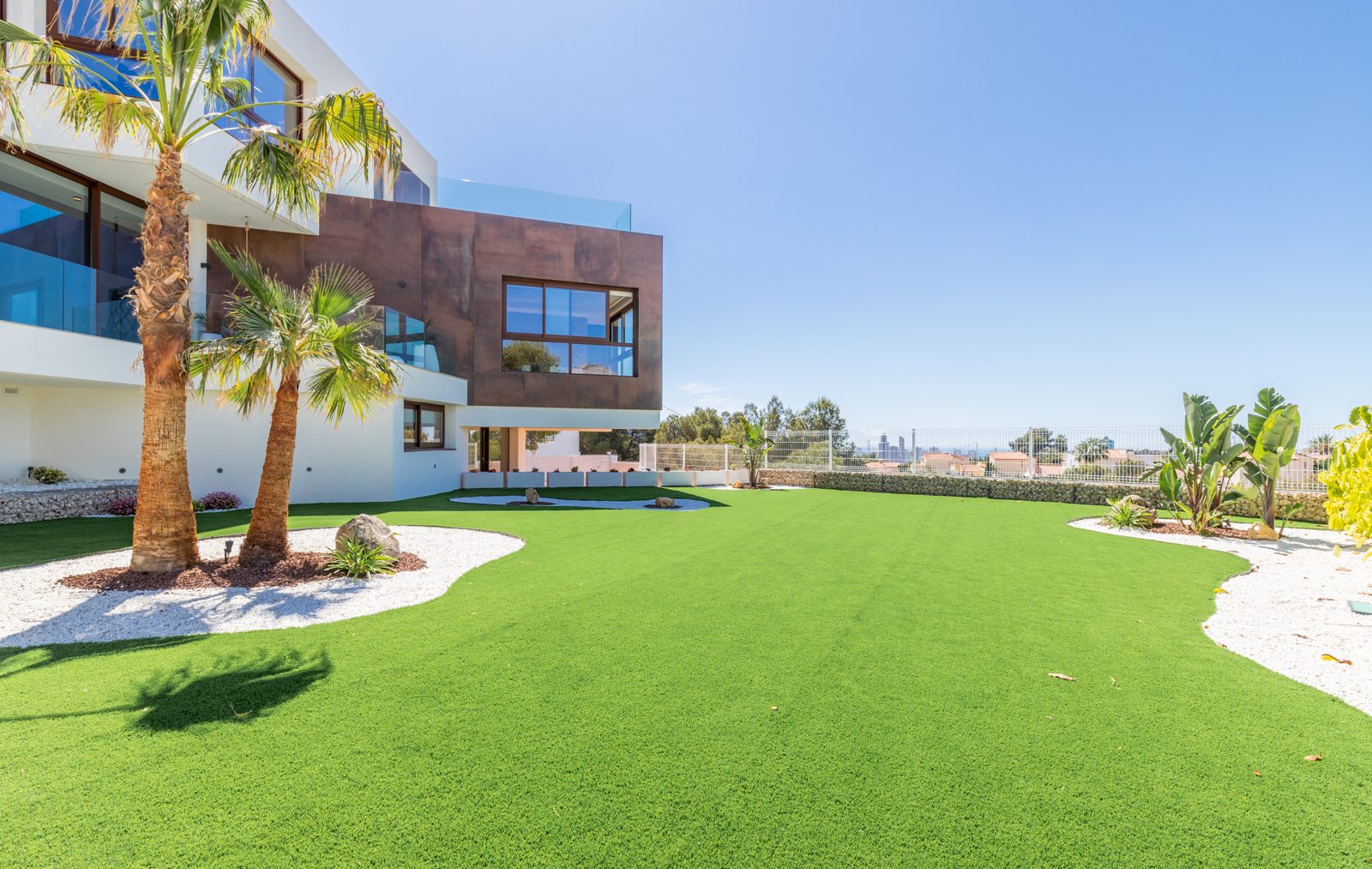 View of the garden featuring artificial turf, palm trees, and a modern facade in La Nucía.