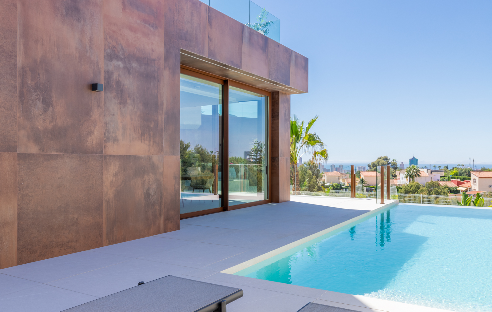 View of the infinity pool with rust-colored panel facade and panoramic city views.