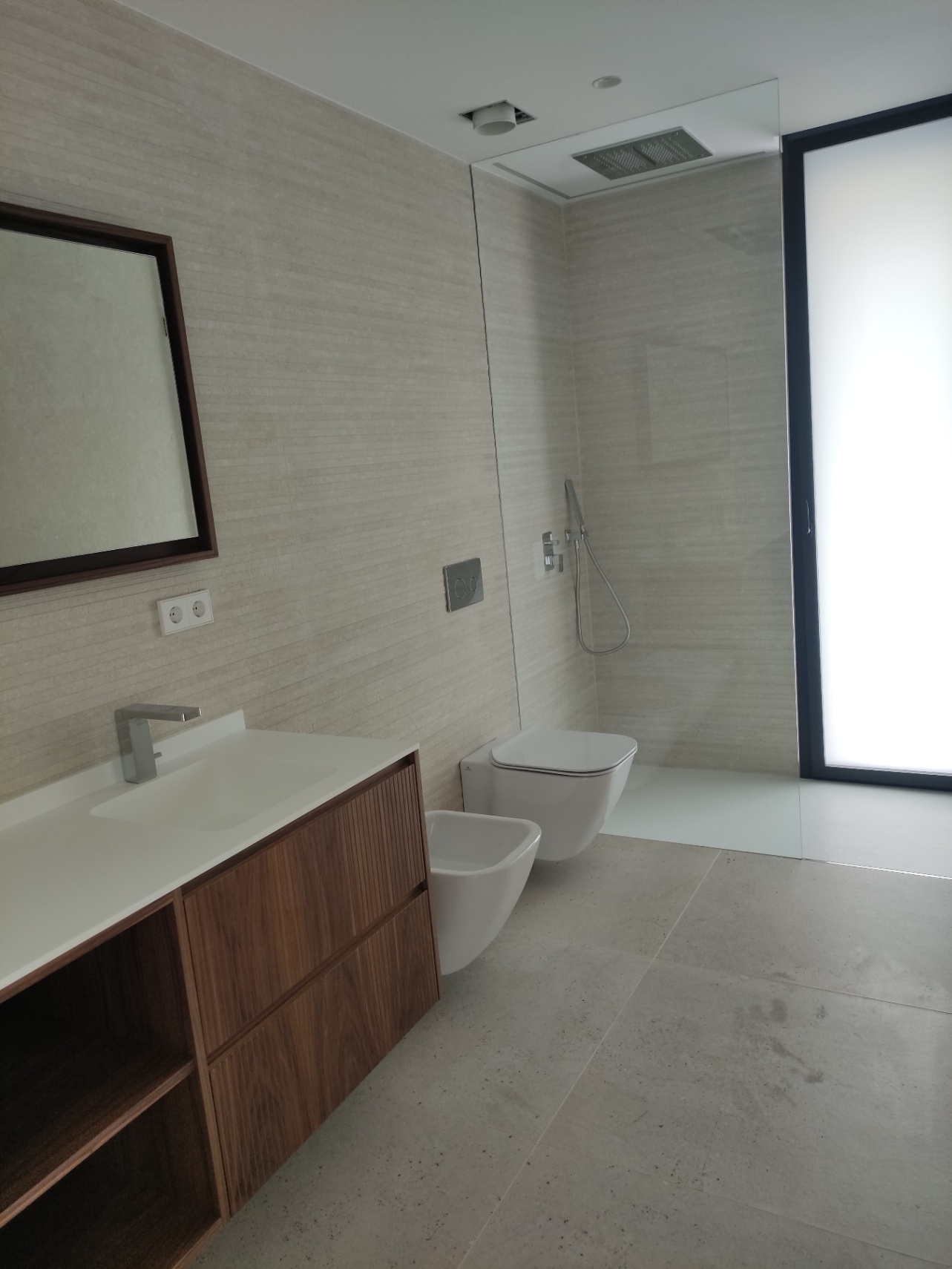 Contemporary bathroom with a walnut-finish vanity, integrated sink, wall-mounted toilet, and a walk-in shower featuring a ceiling-mounted rainfall head.