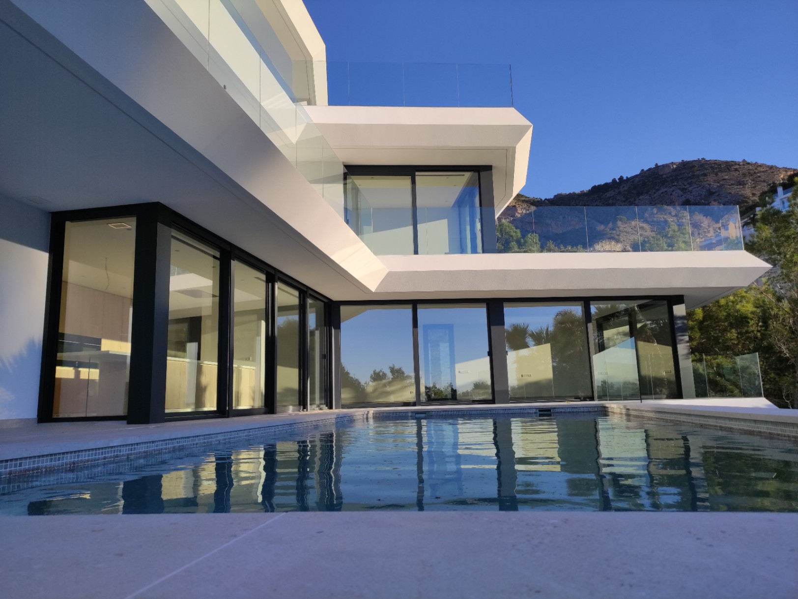 Modern facade featuring floor-to-ceiling black-framed windows and an infinity pool reflecting the geometric architecture against the Altea Hills backdrop.