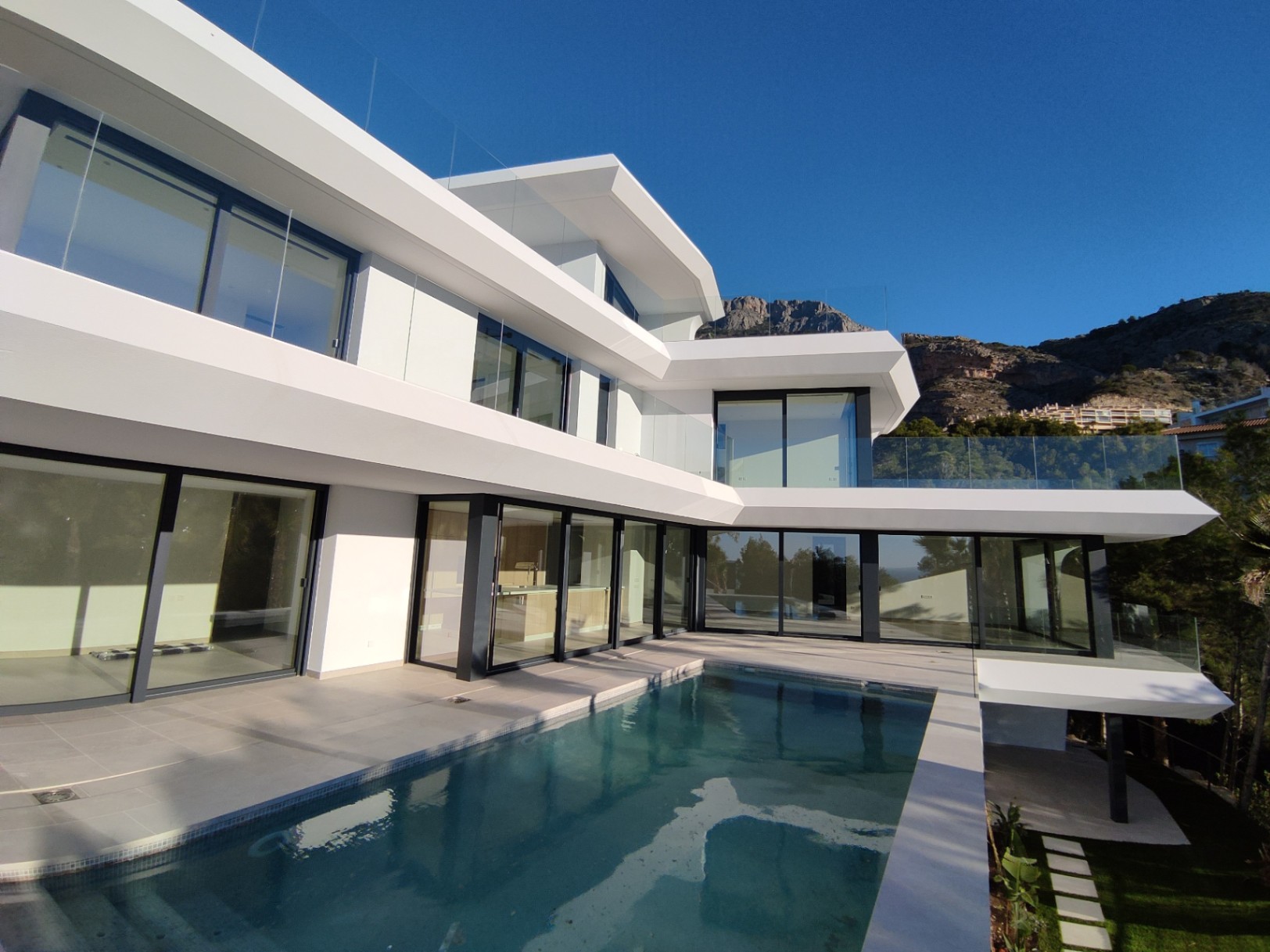 Modern white facade featuring cantilevered levels, floor-to-ceiling glass walls, and a private infinity pool set against a dramatic mountain backdrop.