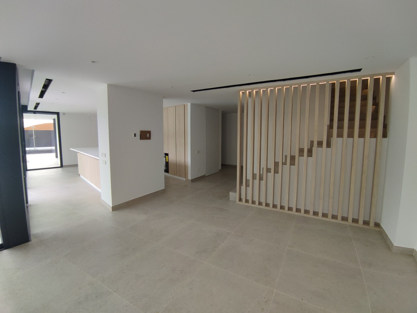 Open-plan living space with large-format porcelain flooring and a minimalist staircase featuring vertical wooden slats and integrated LED lighting.