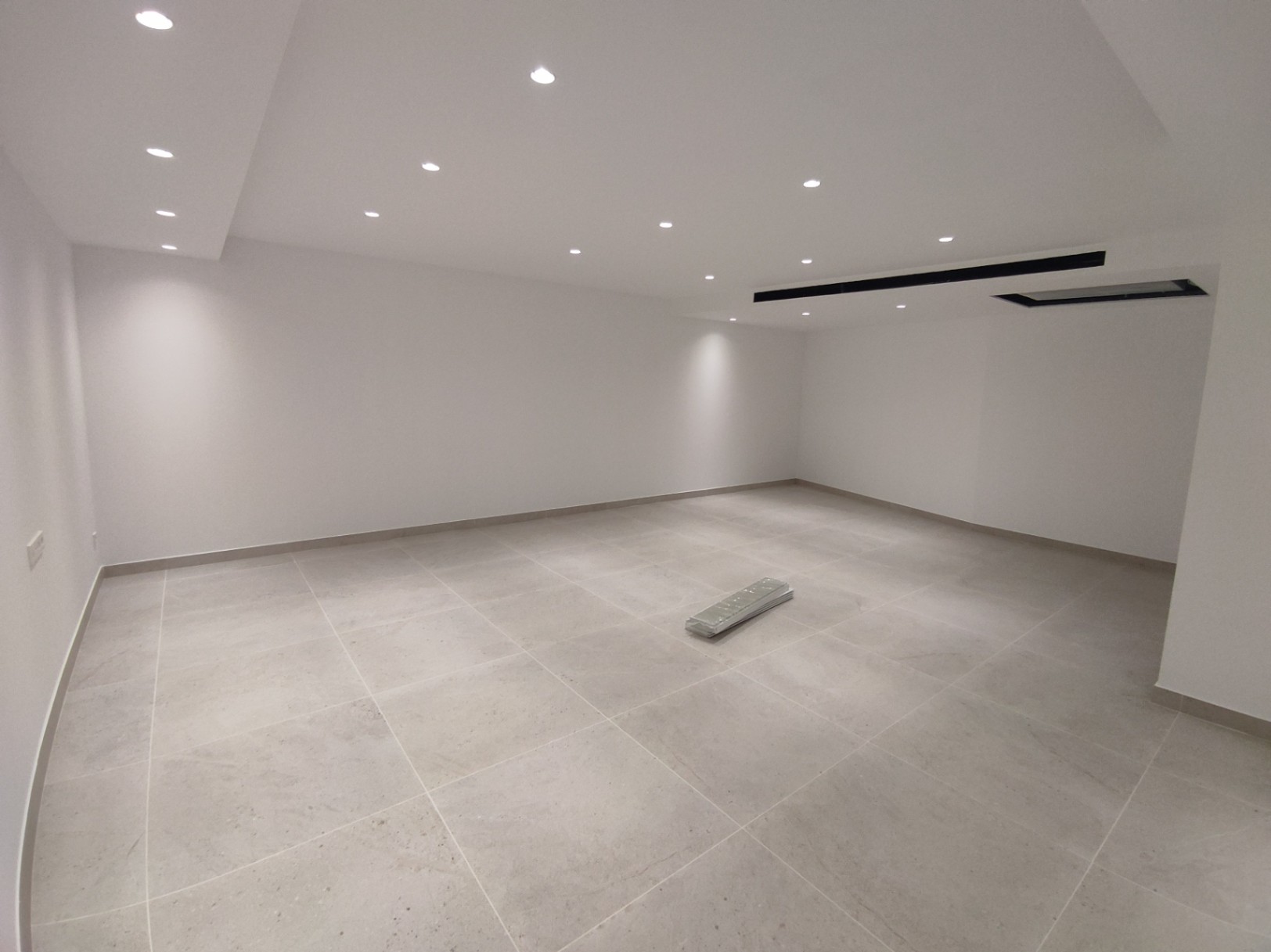 Spacious open-plan room featuring large-format porcelain floor tiles, minimalist white walls, and integrated recessed LED ceiling lighting.