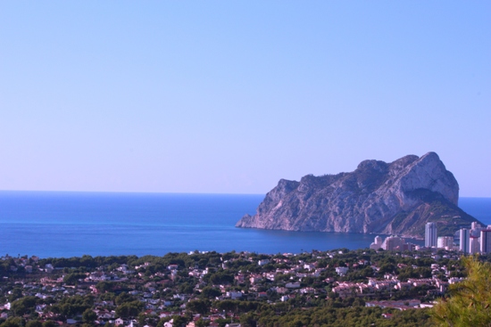 Panoramic view of the Peñón de Ifach and the Mediterranean Sea, showcasing the coastal skyline of Calpe and lush green surroundings under a clear sky.
