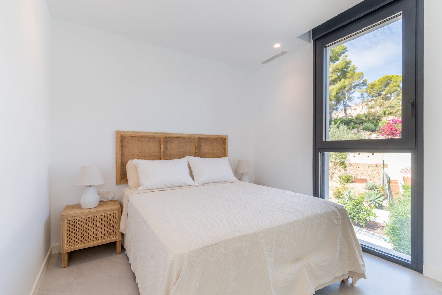 Bright bedroom features a rattan headboard and garden views from the black-framed window.