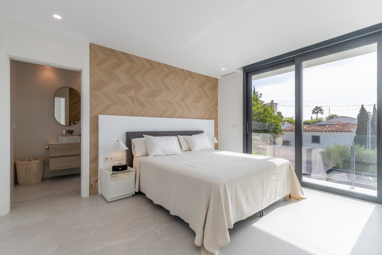 Bright bedroom with herringbone accent wall and ensuite access. Window wall with exterior views.