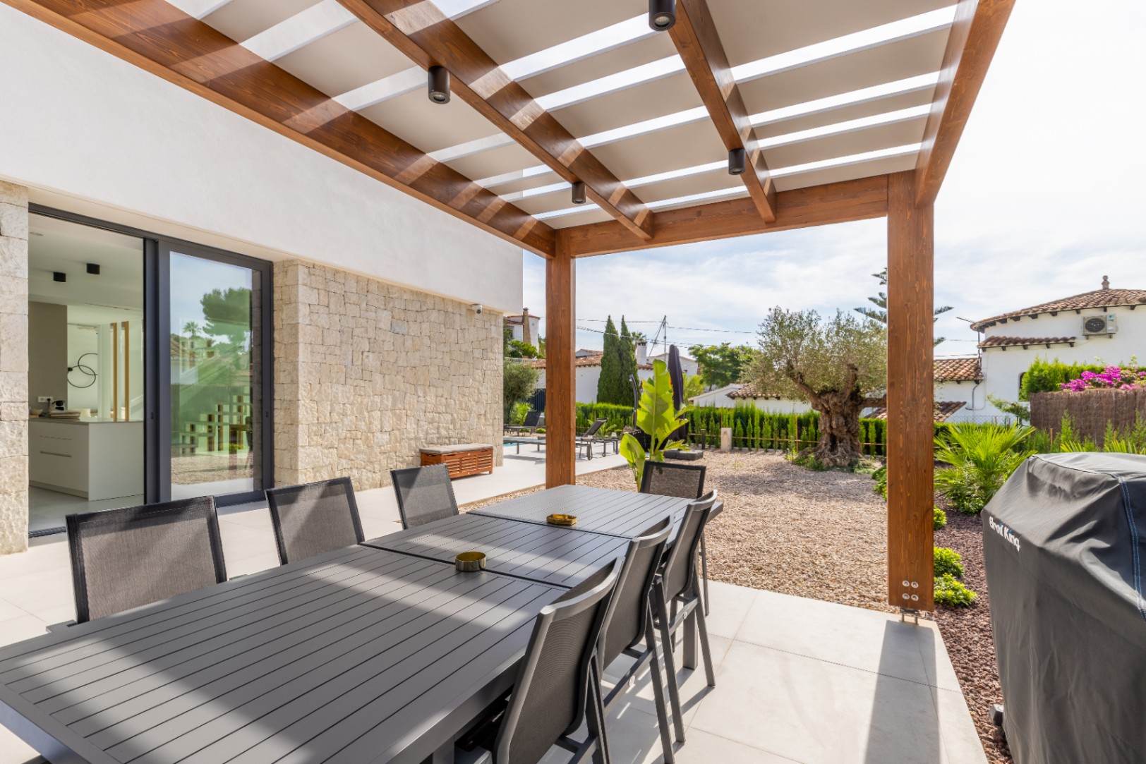 Covered outdoor dining area with wooden pergola and views of the Mediterranean garden.