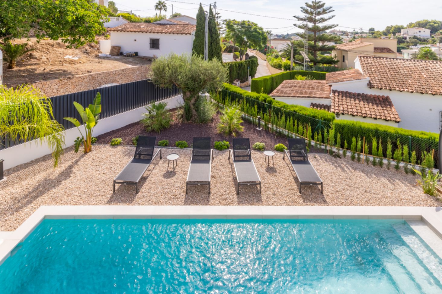 Elevated view of the pool with sun loungers, gravel and hedged garden in Benissa.
