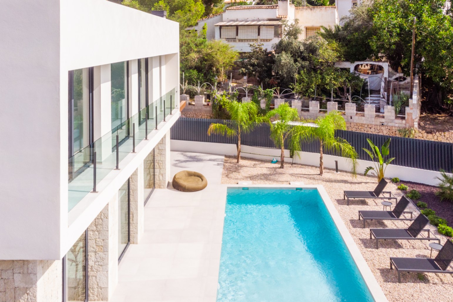 Elevated view of the private pool with sun loungers and gravel garden with young palm trees.